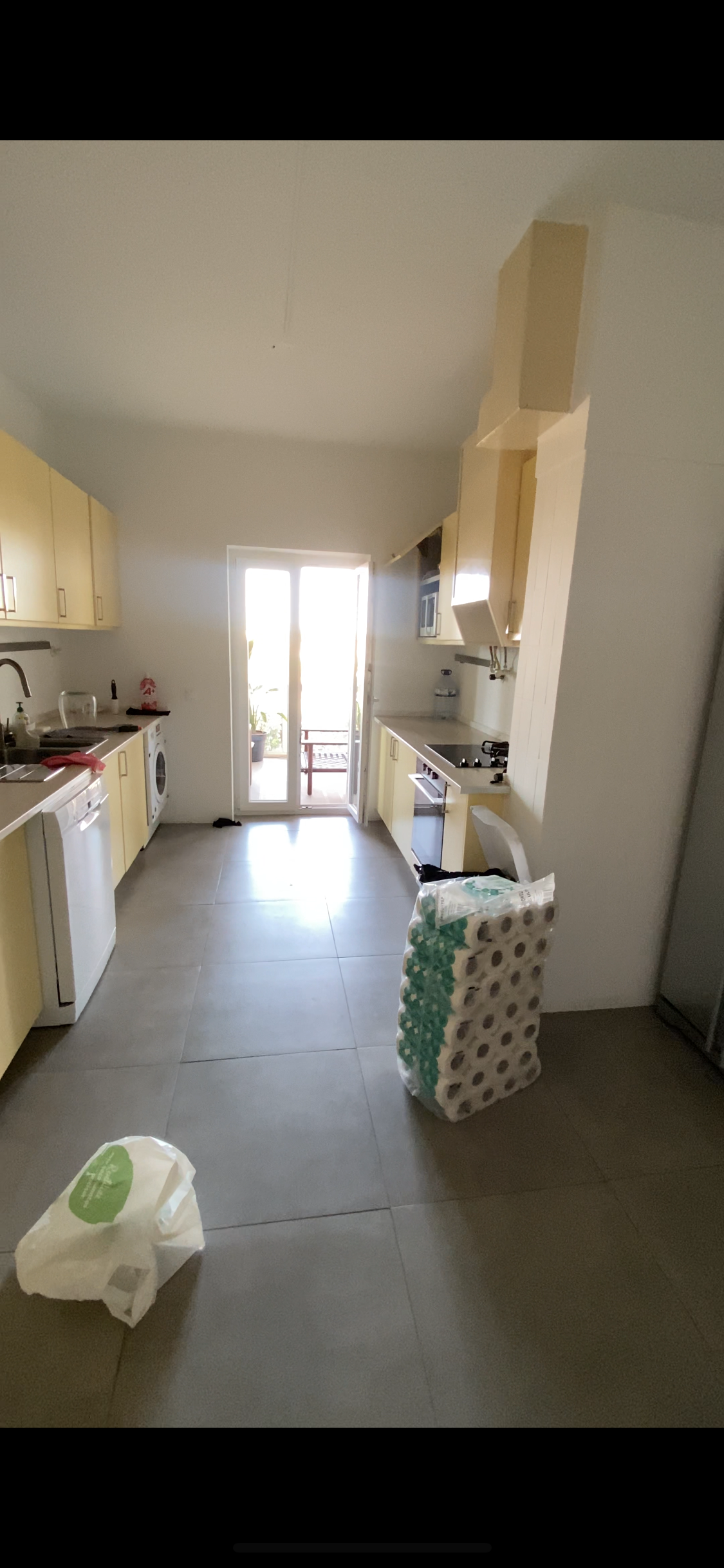 Uma cozinha com armários de cores claras, piso cinza e uma porta que dá para um espaço ao ar livre.