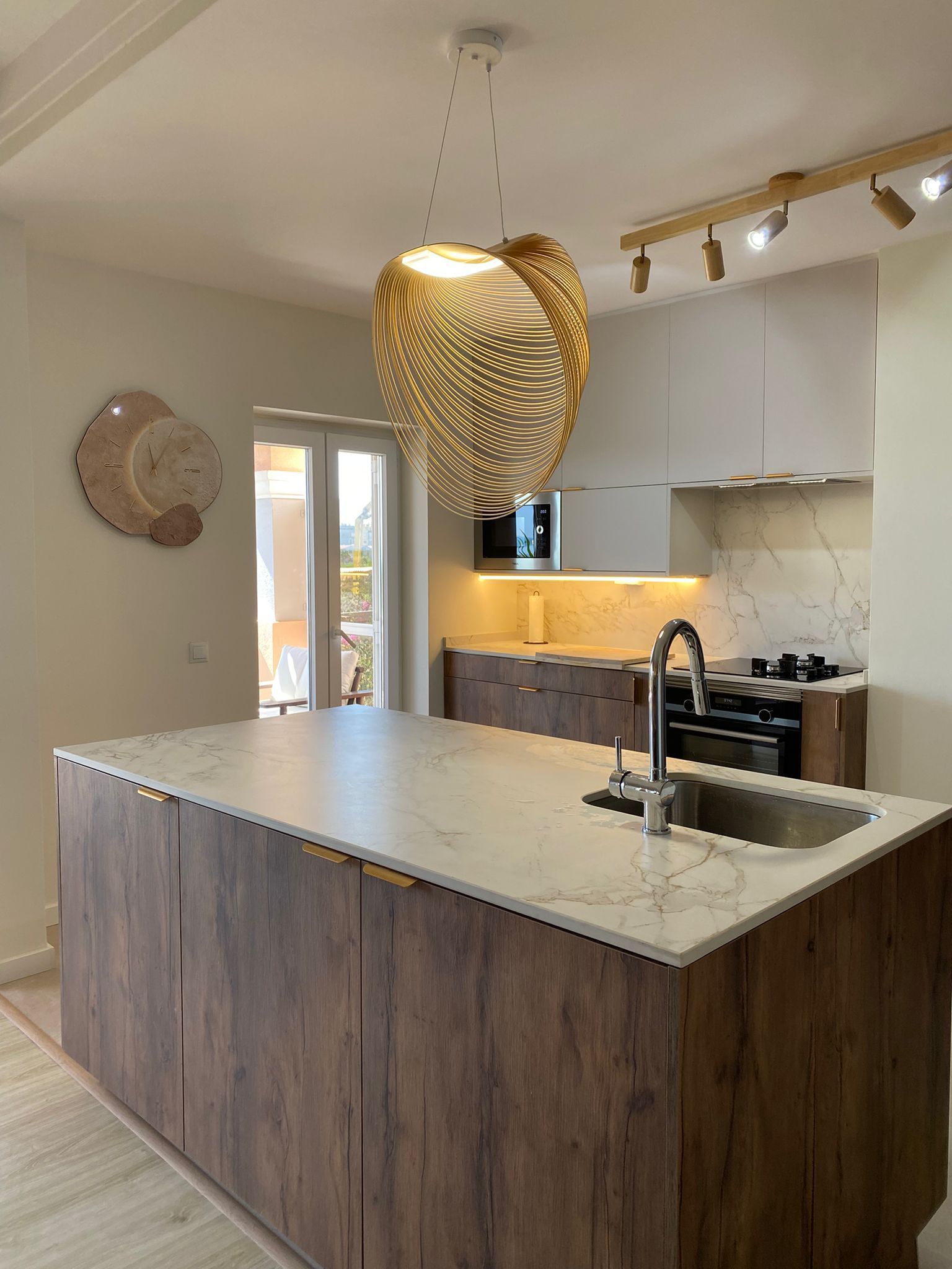 Cozinha moderna com armários que imitam madeira, ilha de bancada branca, luminária pendente e placas de parede decorativas.
