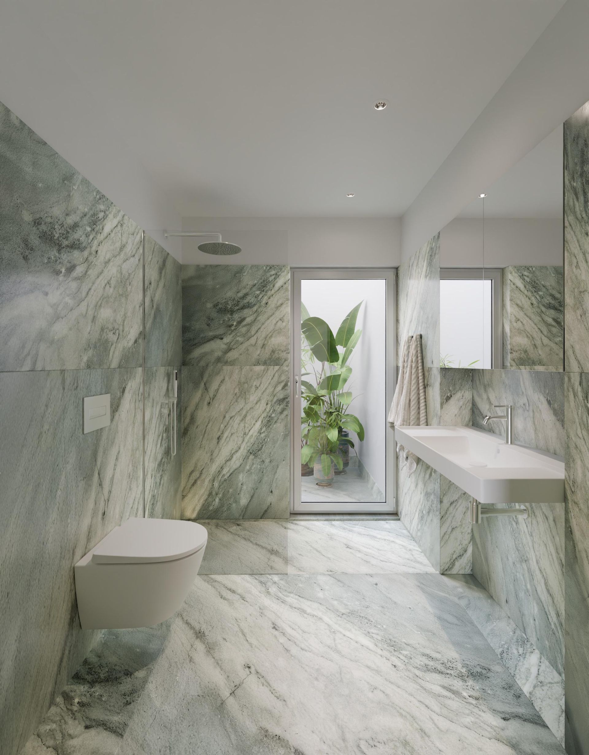 Banheiro moderno com azulejos de mármore, pia suspensa, vaso sanitário e porta de vidro com vista para a área verde externa.