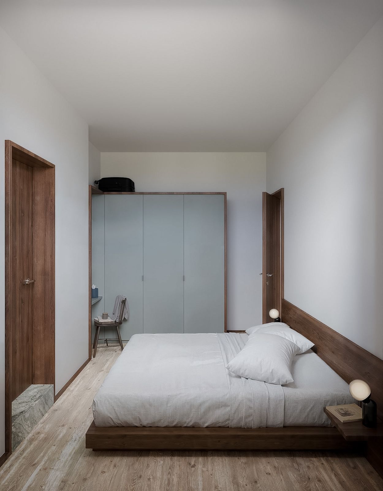 Quarto minimalista com cama branca, guarda-roupa cinza, portas de madeira e paredes brancas lisas.