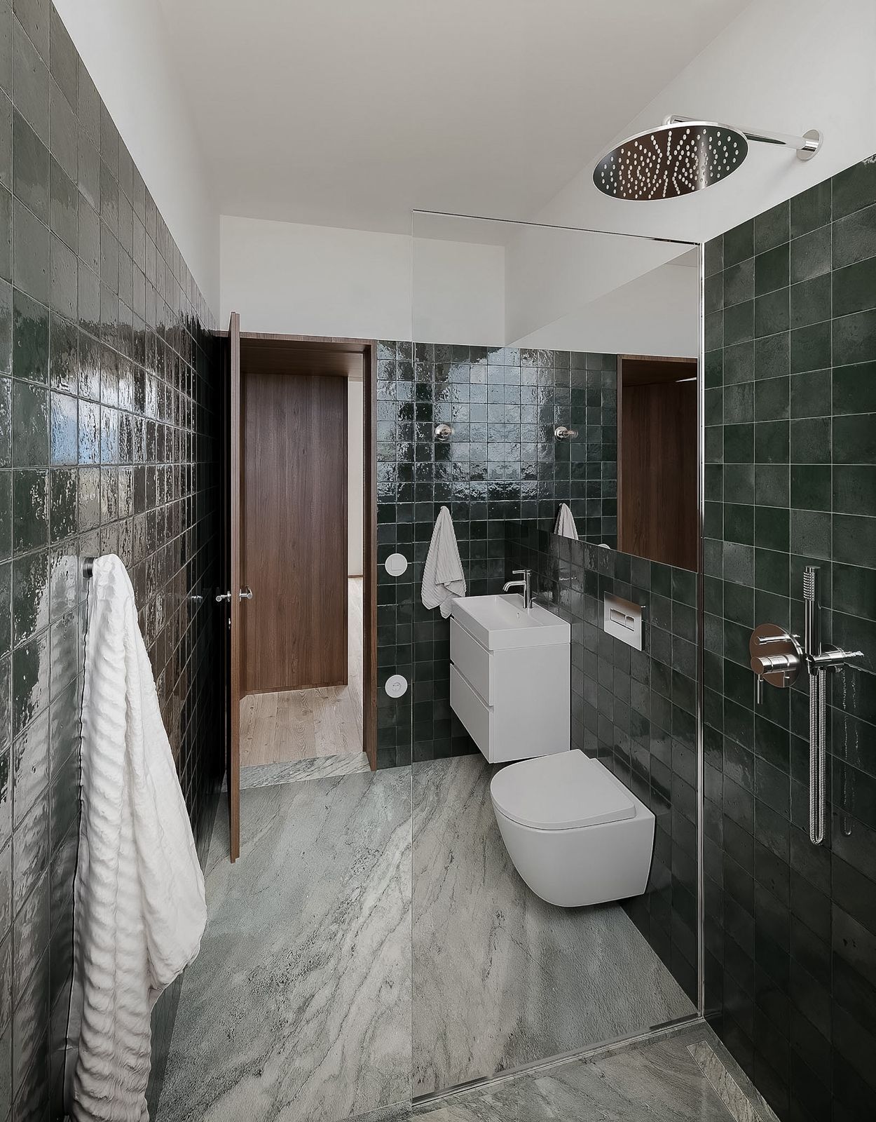 Banheiro moderno com box de azulejos escuros, pia branca e vaso sanitário ao lado de um grande espelho.