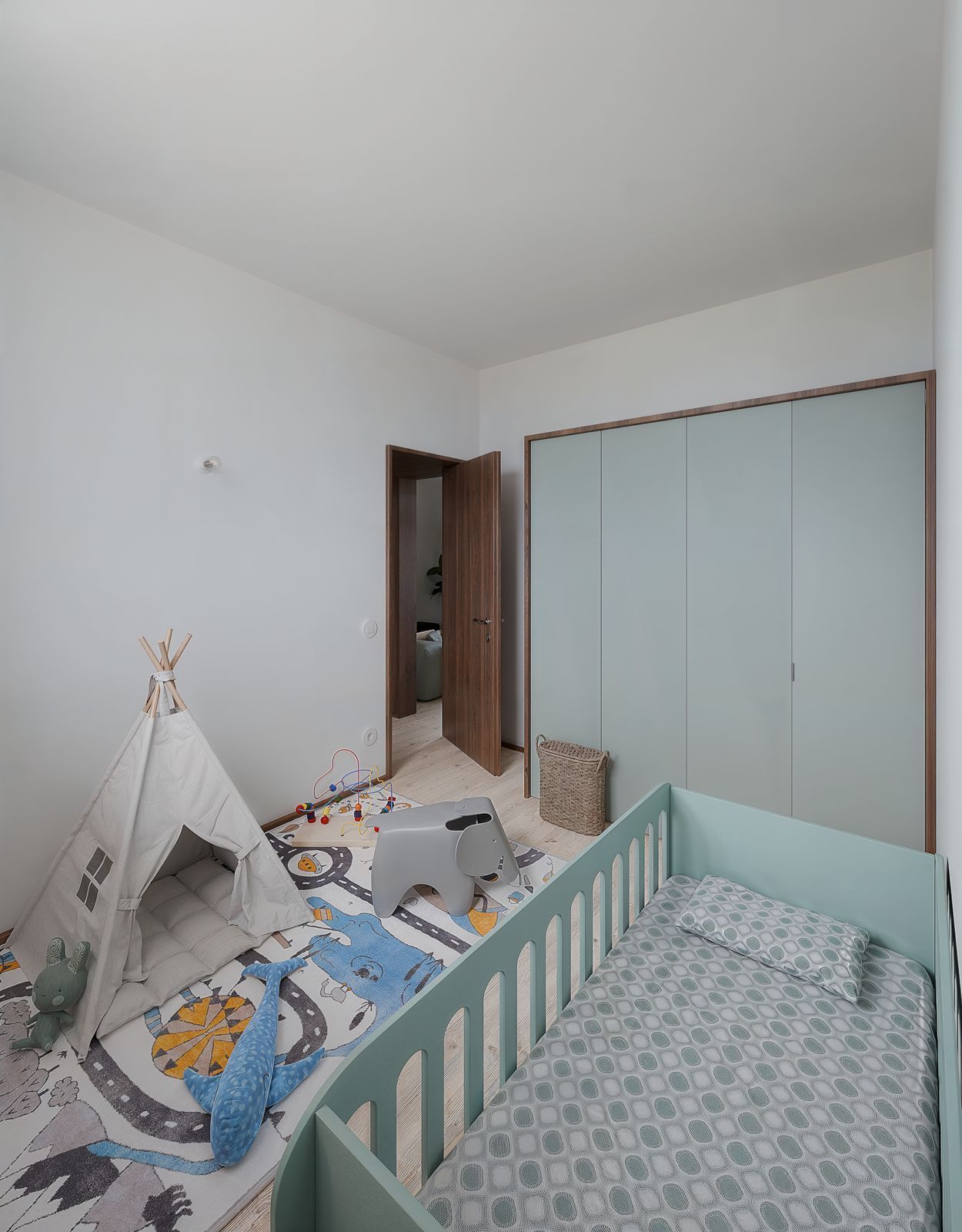 Quarto de bebê com berço, tenda de brincar em formato de tipi e guarda-roupa grande em um ambiente claro e branco.