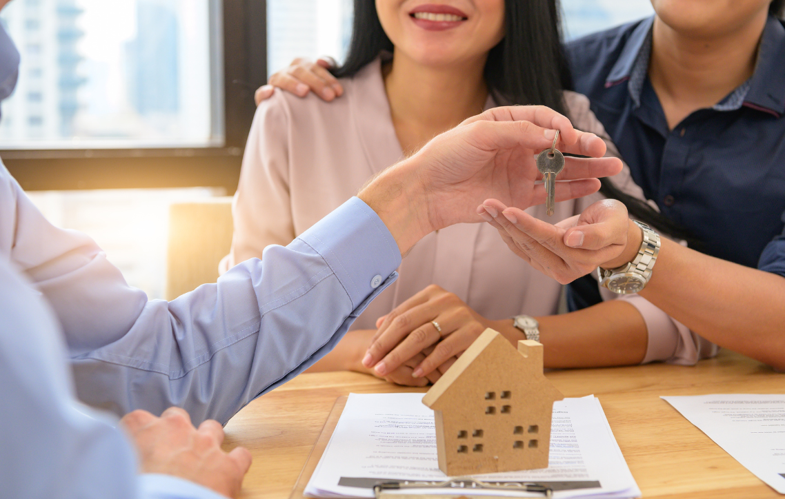 Hands exchanging house keys over a contract at a real estate meeting table