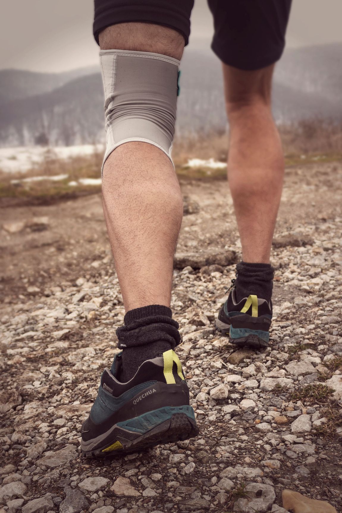 Una persona indossa un tutore medico nero per il braccio, una fascia e un reggiseno sportivo a fantasia e pantaloncini sportivi verde oliva.