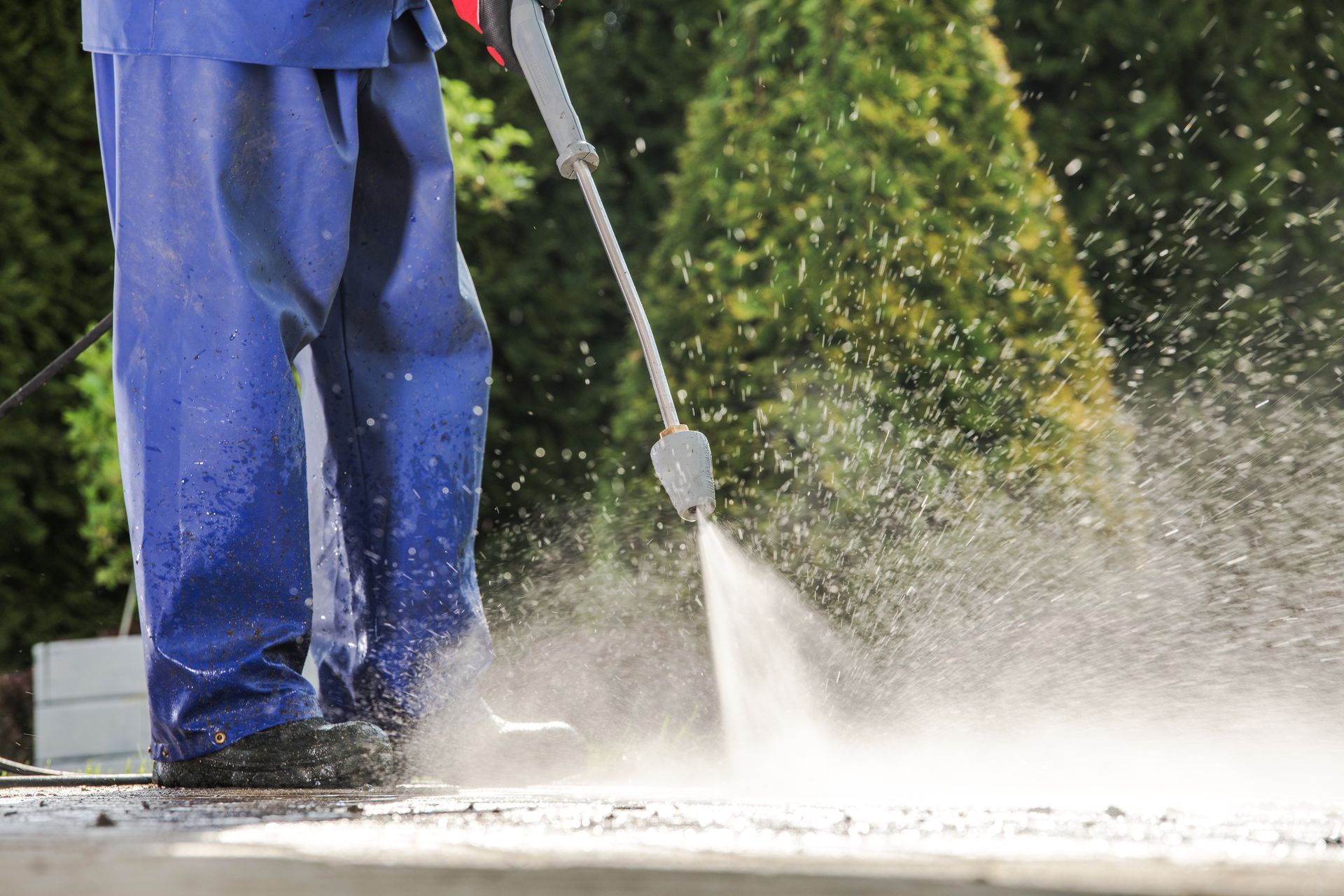 Person power washing a paved surface, spraying water into the air.