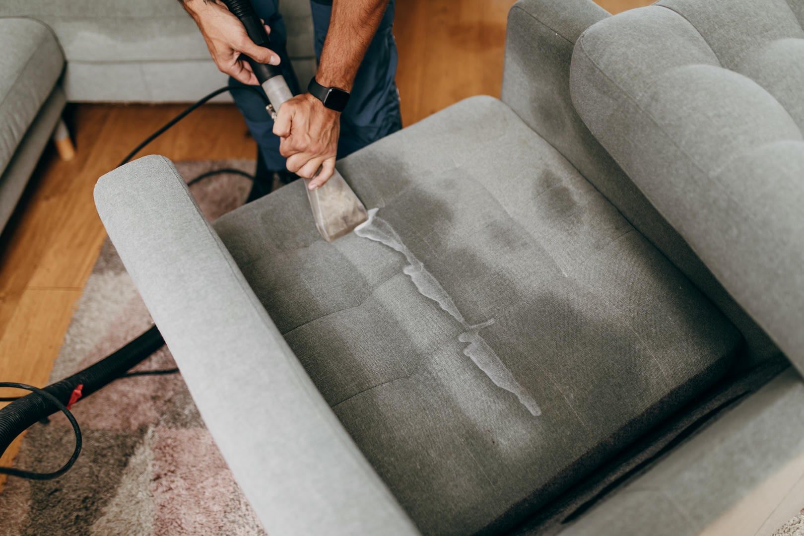 Person cleaning a grey sofa with a cleaning machine.