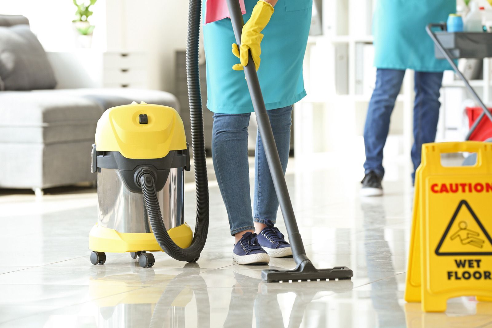 Person vacuuming a floor near a yellow