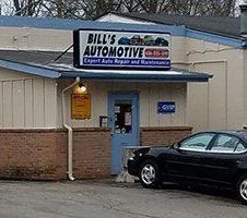 Small auto repair shop with a blue door and a black car parked outside.