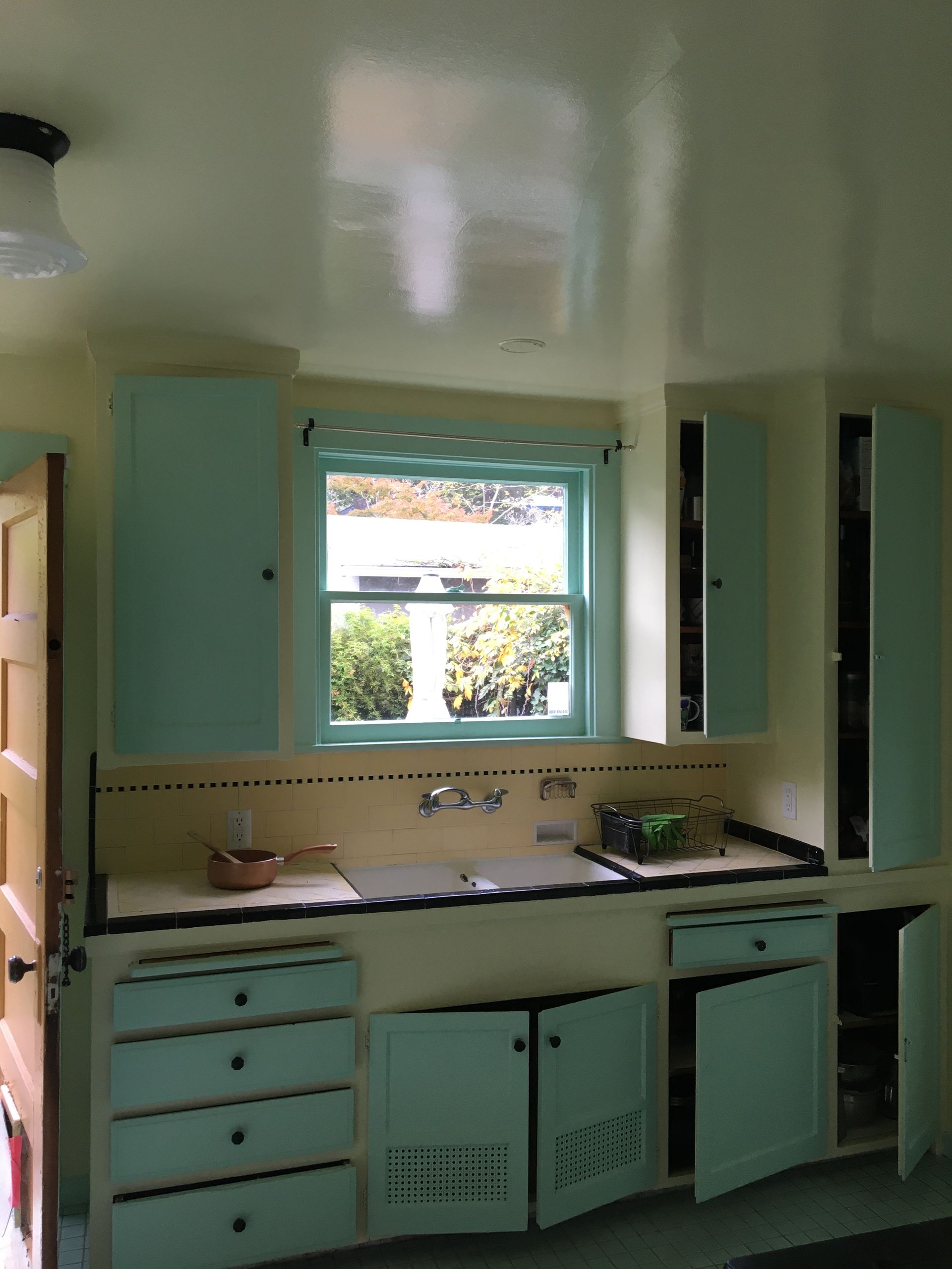 A person in blue overalls painting a white border on a teal wall in a room.