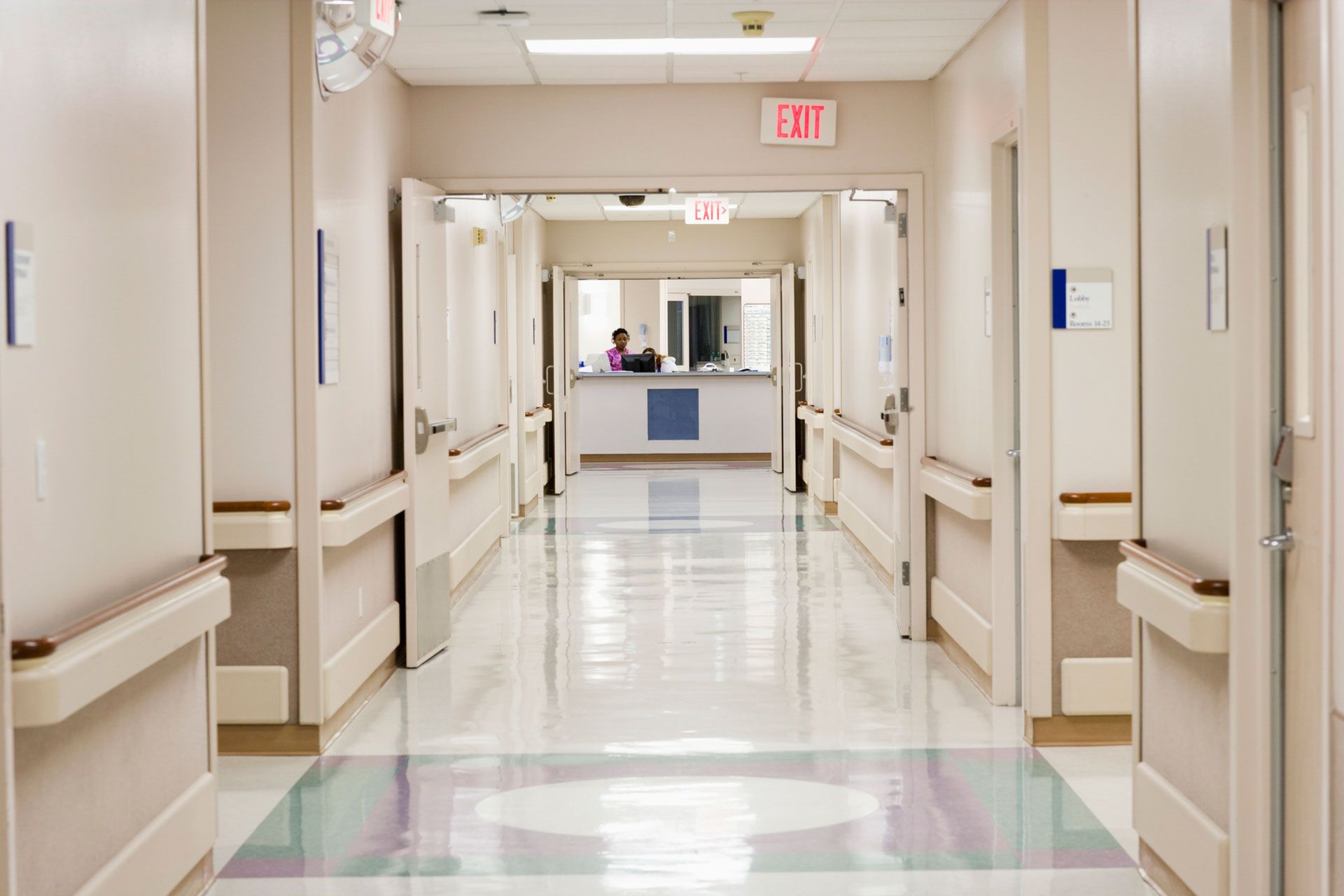 An empty hospital hallway with a red exit sign