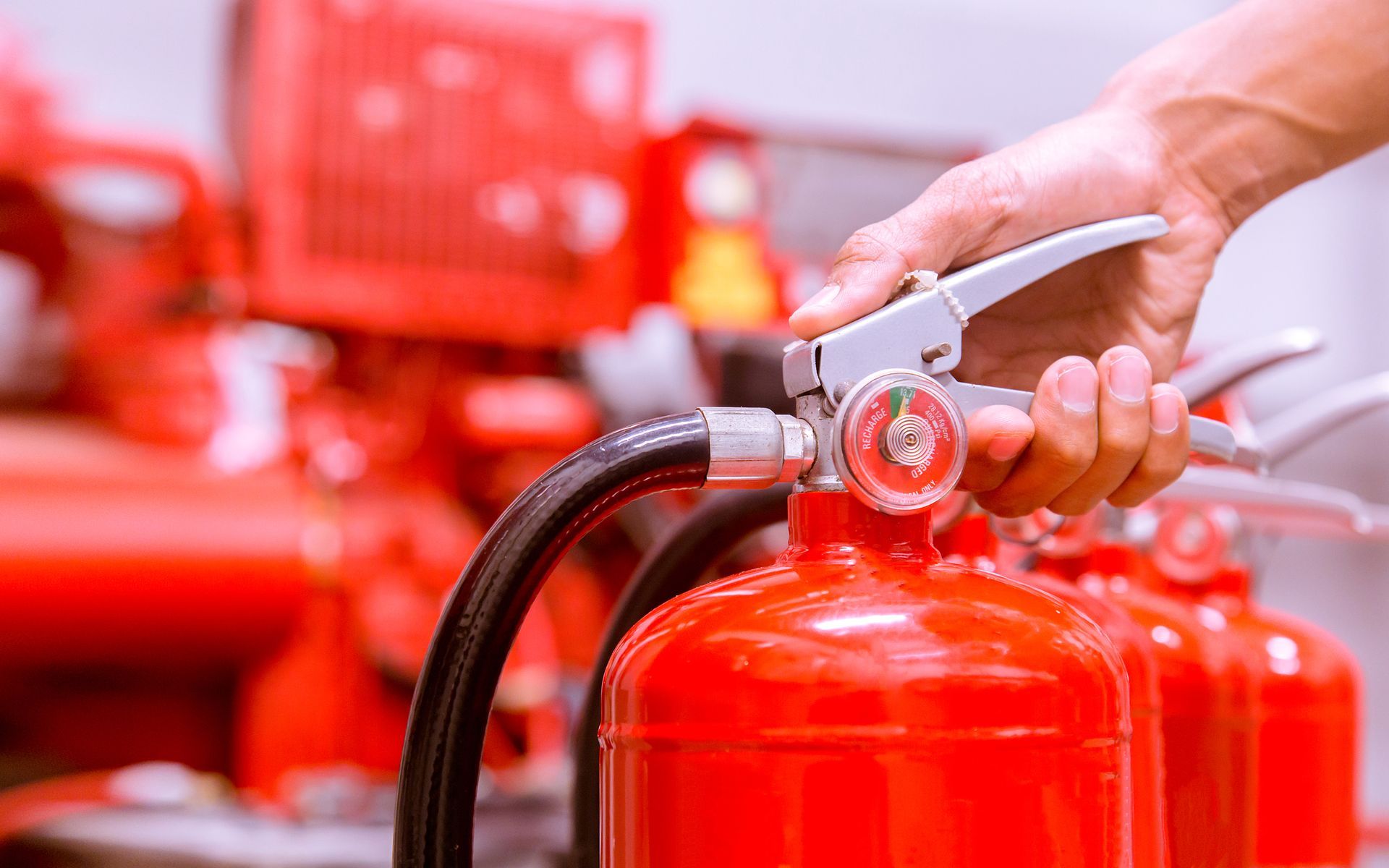 Closeup of hand holding fire extinguisher from its metallic handle, showcasing fire protection.