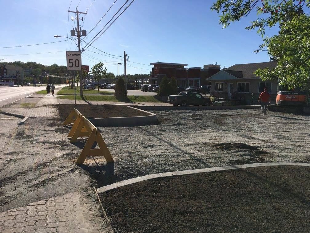 Chantier routier : gravier, barrières et panneau de limitation de vitesse. Deux personnes marchent près d’un commerce par une journée ensoleillée.