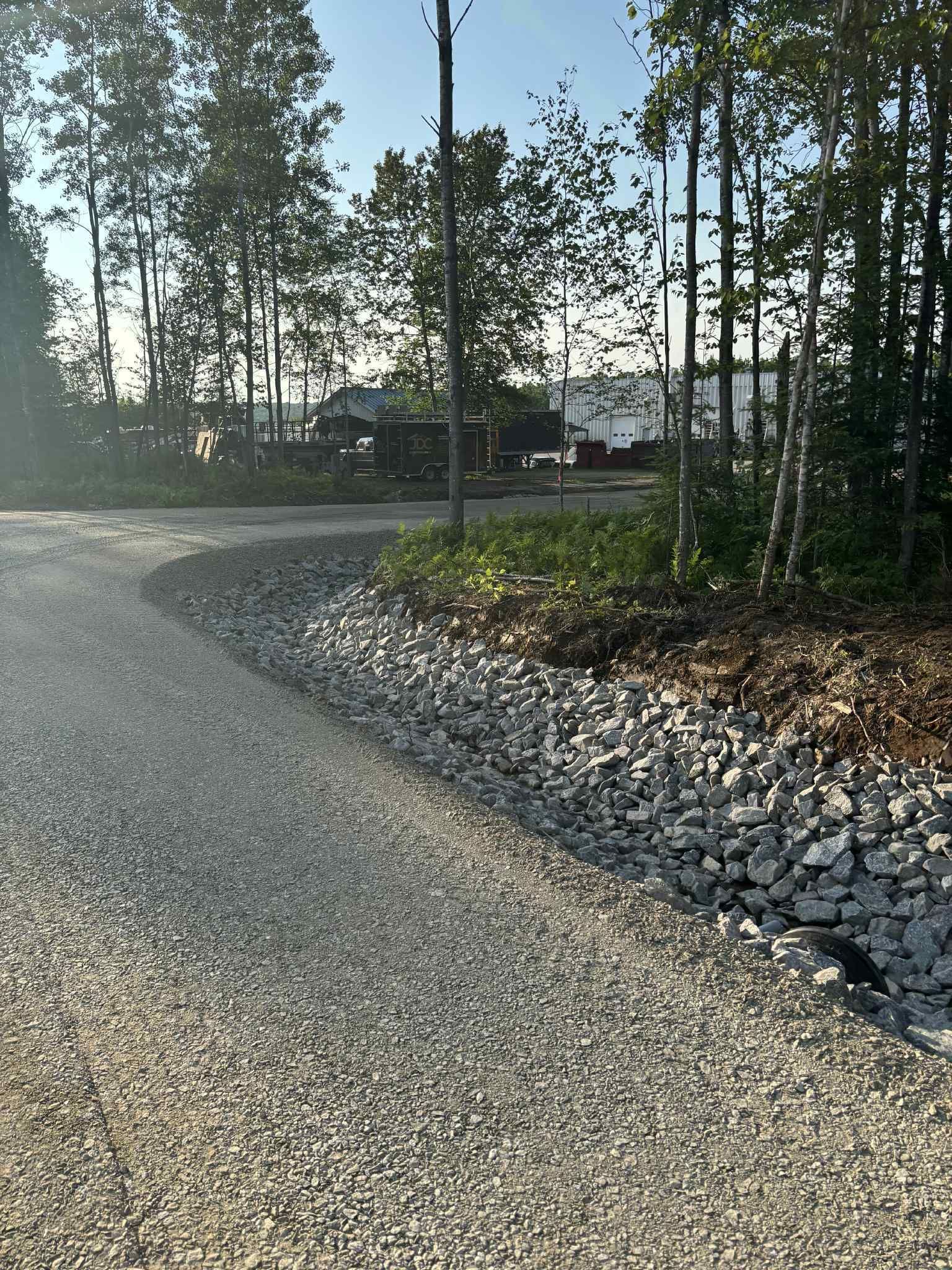 Un chemin de gravier décrit une courbe vers la droite, bordé de rochers, avec des arbres en arrière-plan ; journée ensoleillée.