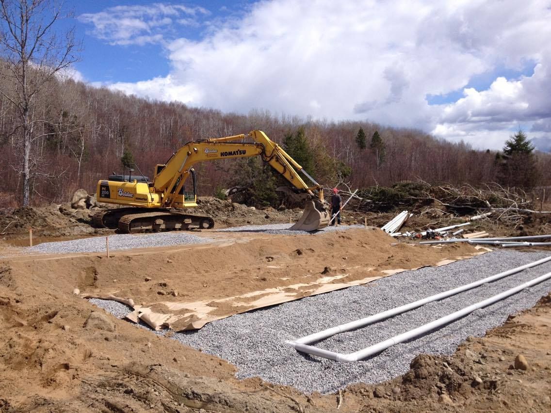 Une pelleteuse jaune creuse sur un chantier de construction avec du gravier et des tuyaux.