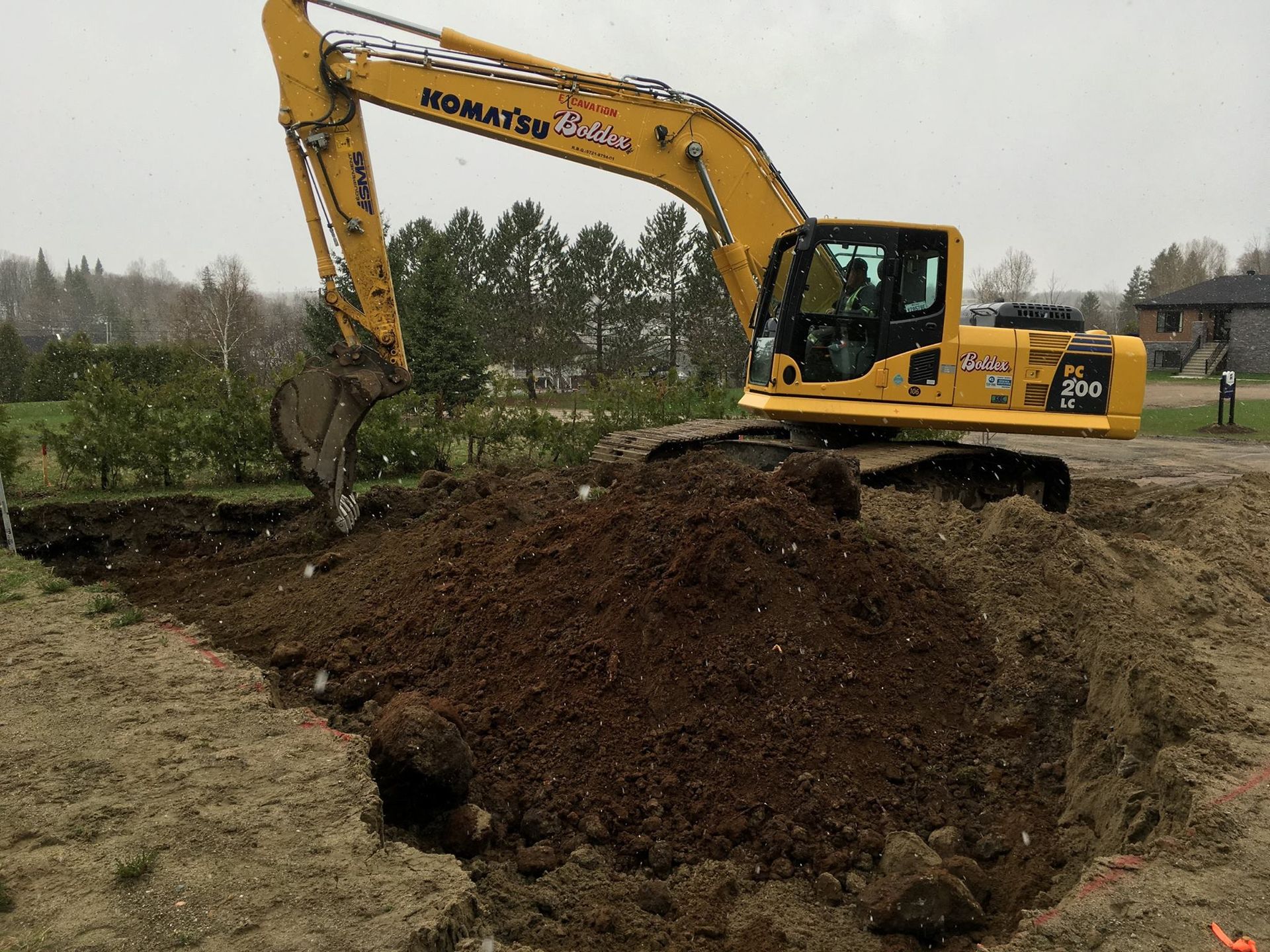 Une pelle Komatsu jaune creuse une tranchée, un tas de terre brune, en extérieur.
