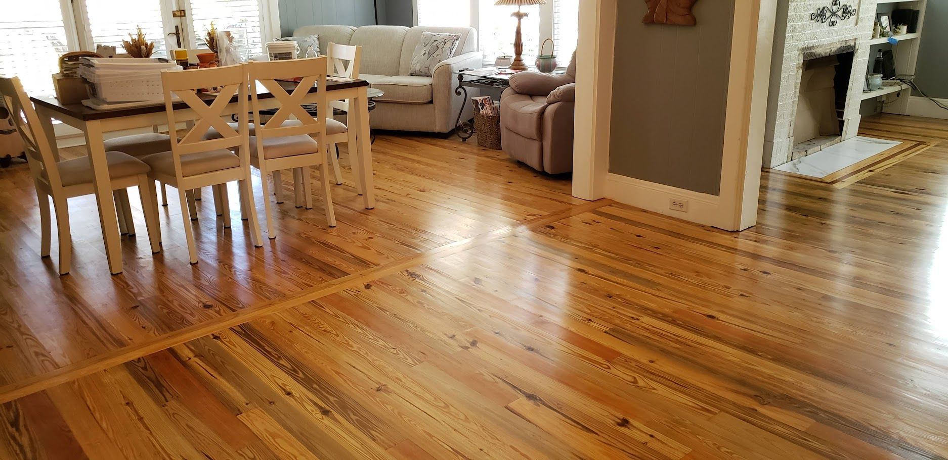 Spacious dining and living room with polished hardwood floors, wooden table, chairs, sofa, and fireplace.