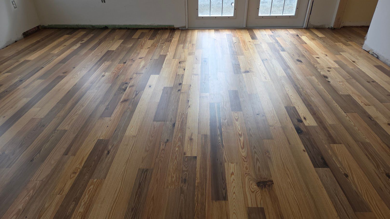 Empty room with light wood plank flooring and sunlight near a windowed door
