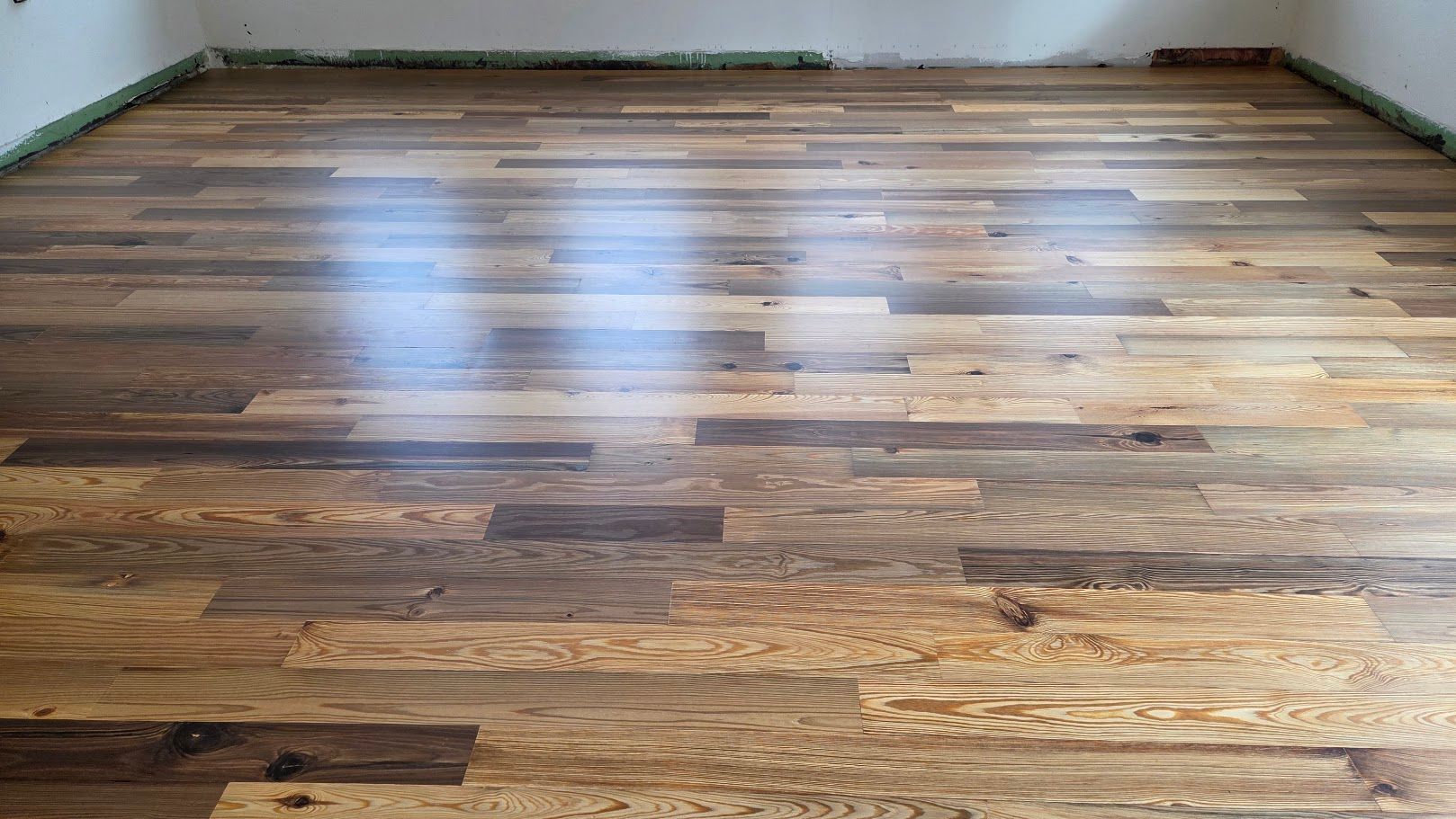 Empty room with polished hardwood floor and white walls, seen from a low angle.