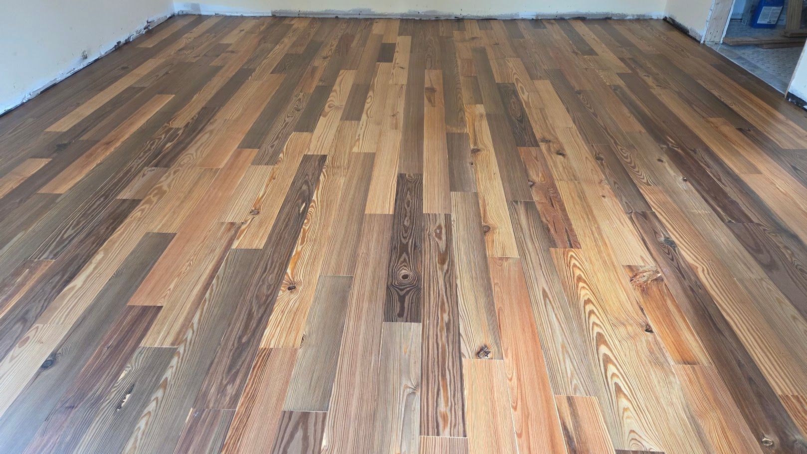 Empty room with wide-plank wood flooring in varied brown tones, viewed from floor level.