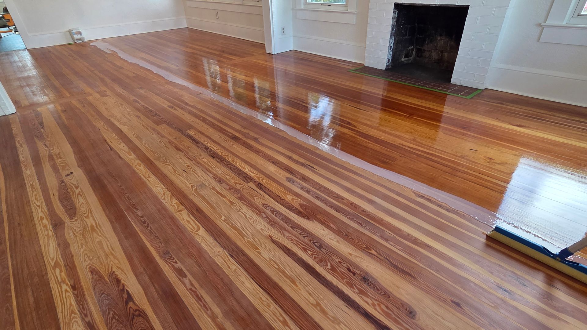 Newly refinished glossy hardwood flooring with a visible line between the sealed and unsealed sections of a room.