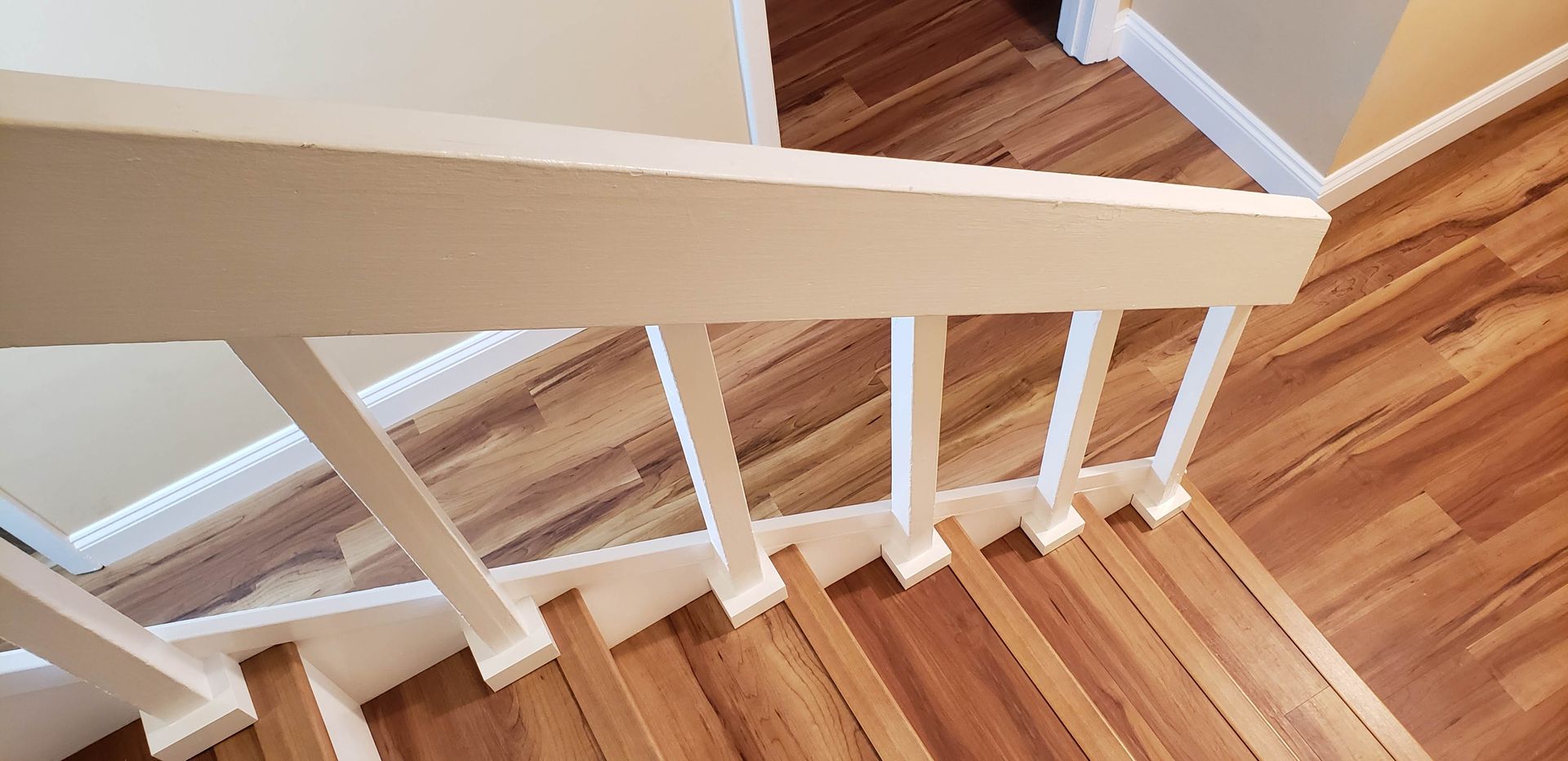 A wooden staircase with white painted balusters and a handrail, viewed from above looking down the steps.
