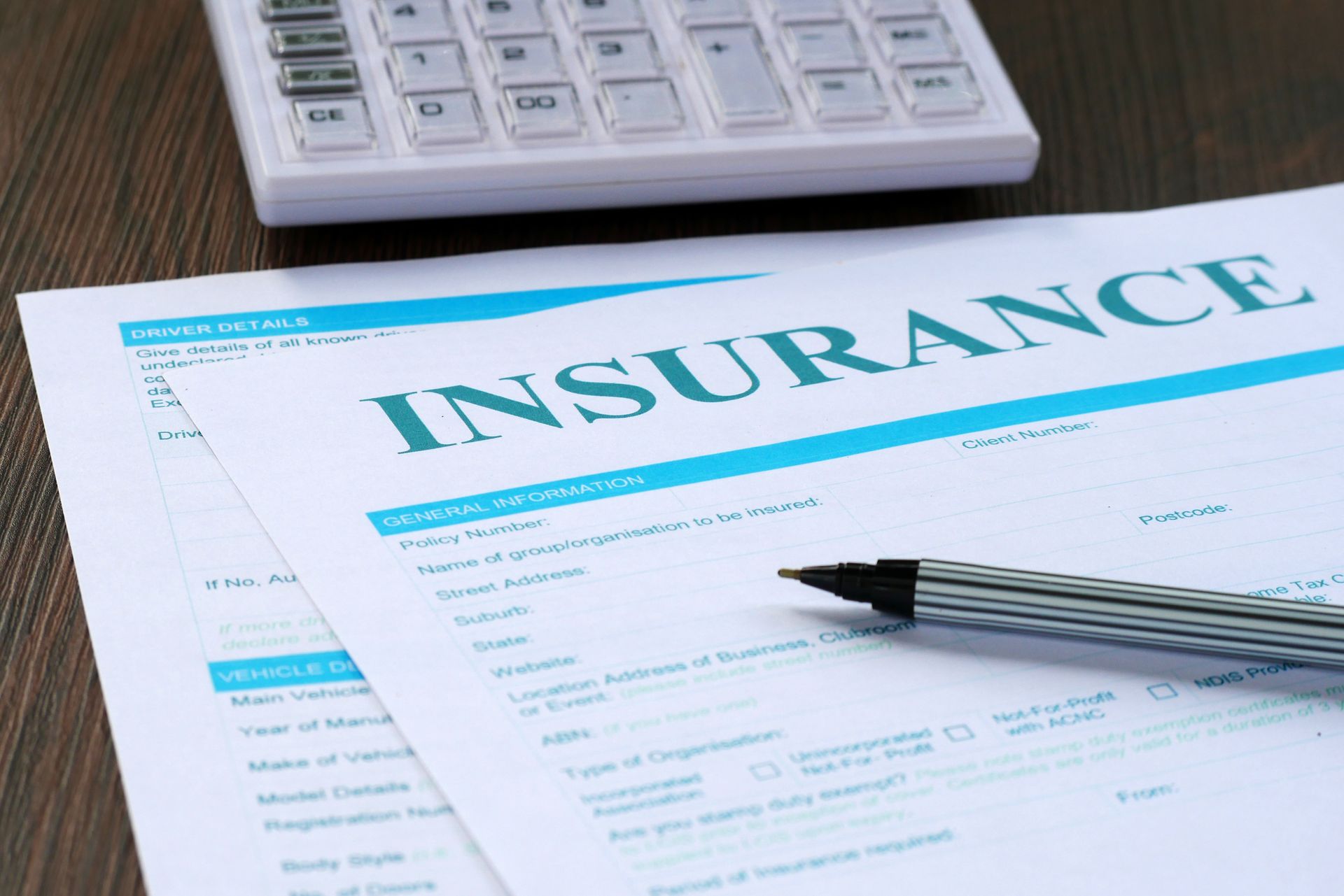 A pen is sitting on top of an insurance form next to a calculator.