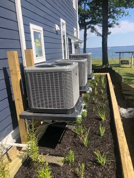 Outdoor HVAC units beside a blue house with a garden bed and ocean view