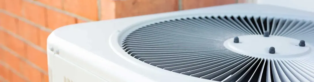 White outdoor air conditioner unit beside an orange brick wall