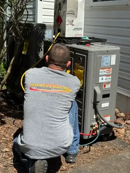 Worker kneeling beside an open outdoor HVAC unit, servicing wiring and components.