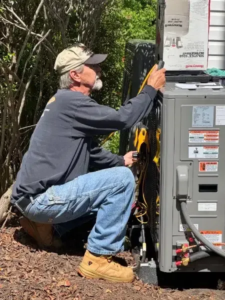 Worker kneeling beside an outdoor HVAC unit, adjusting wiring with tools