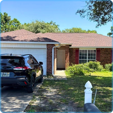 Single-story brick house with white garage, black SUV in driveway, and front lawn on a sunny day