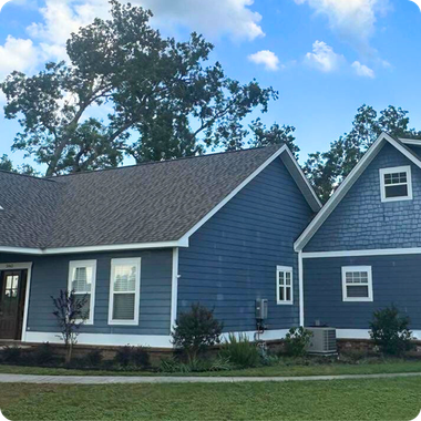 Blue house with white trim and a small gabled wing, set on a grassy lawn under a partly cloudy sky