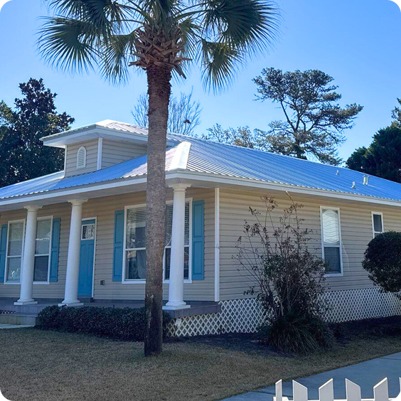 Blue house with white trim and columns, palm tree in front, under a clear sky