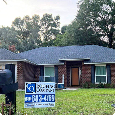 Brick house with a blue roof and a roofing company yard sign in the front lawn.