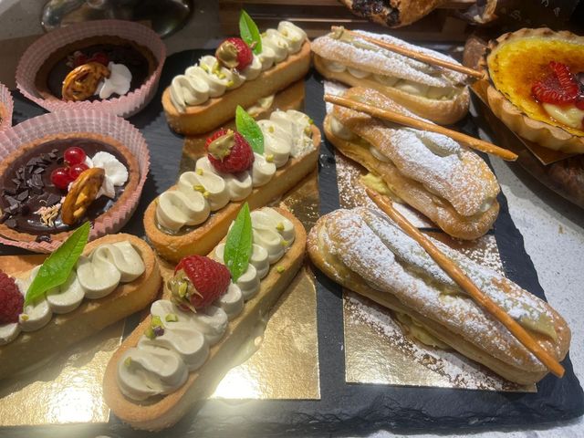 Un assortimento di pasticcini su un vassoio, tra cui crostate di frutta, éclair e pasticcini ricoperti di zucchero a velo.