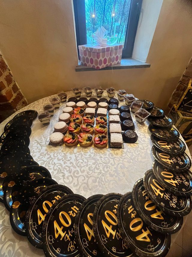 Composizione rotonda di palloncini neri e oro per il 40° compleanno, che circondano un assortimento di dolcetti su un tavolo.