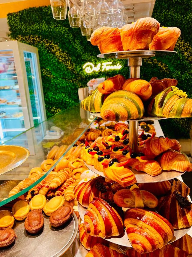 In una pasticceria, un assortimento di pasticcini e croissant è disposto su vassoi a più livelli accanto