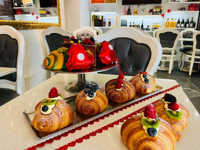 Vassoio di pasticcini assortiti guarniti con fragole e mirtilli, esposto in una vetrina luminosa da caffetteria.