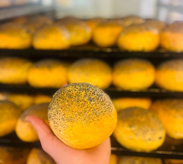 Una mano che regge un panino giallo a pois, con altri panini impilati su vassoi sullo sfondo.