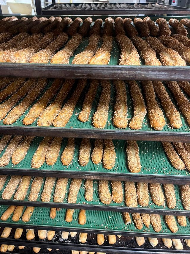 File di cibi fritti dorati su griglie metalliche impilate, probabilmente in fase di raffreddamento in una cucina commerciale.