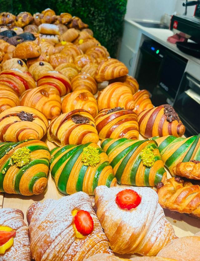 File di croissant e pasticcini colorati esposti in una vetrina da pasticceria.
