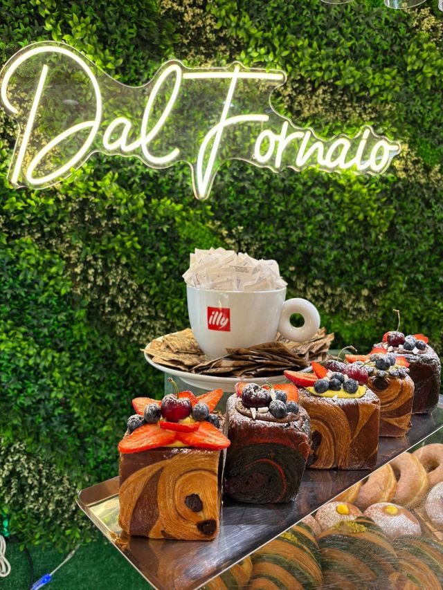 Un assortimento di torte e pasticcini su un vassoio davanti a una parete verde con un'insegna al neon "Dal Fornito".