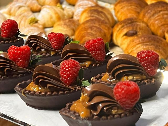 Tartellette al cioccolato con lamponi, caramello e glassa di cioccolato fondente, disposte su un vassoio.