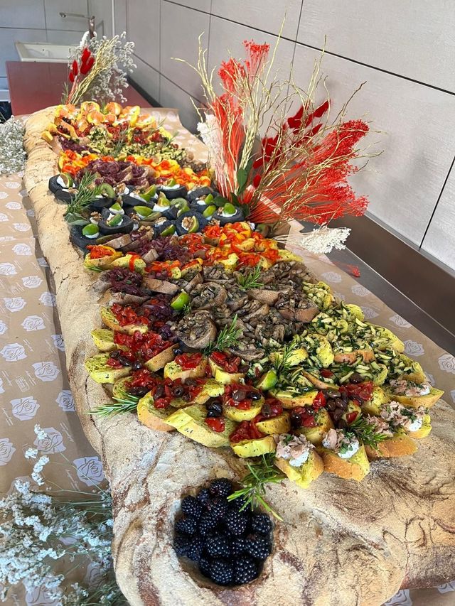 Un grande vassoio di pasticcini e frutta assortiti su un tavolo, decorato con composizioni floreali rosse e bianche.