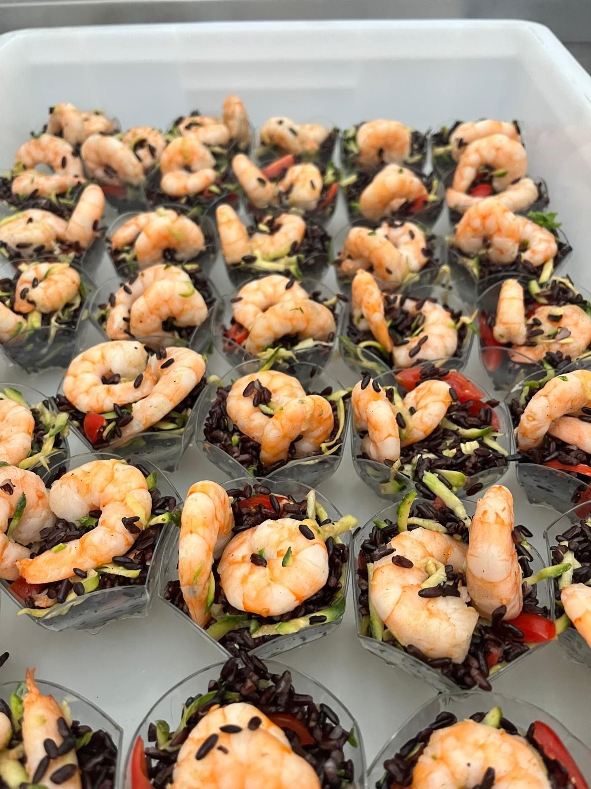 Rotoli di sushi di gamberi disposti in file su un vassoio, guarniti con semi di sesamo e altri ingredienti.