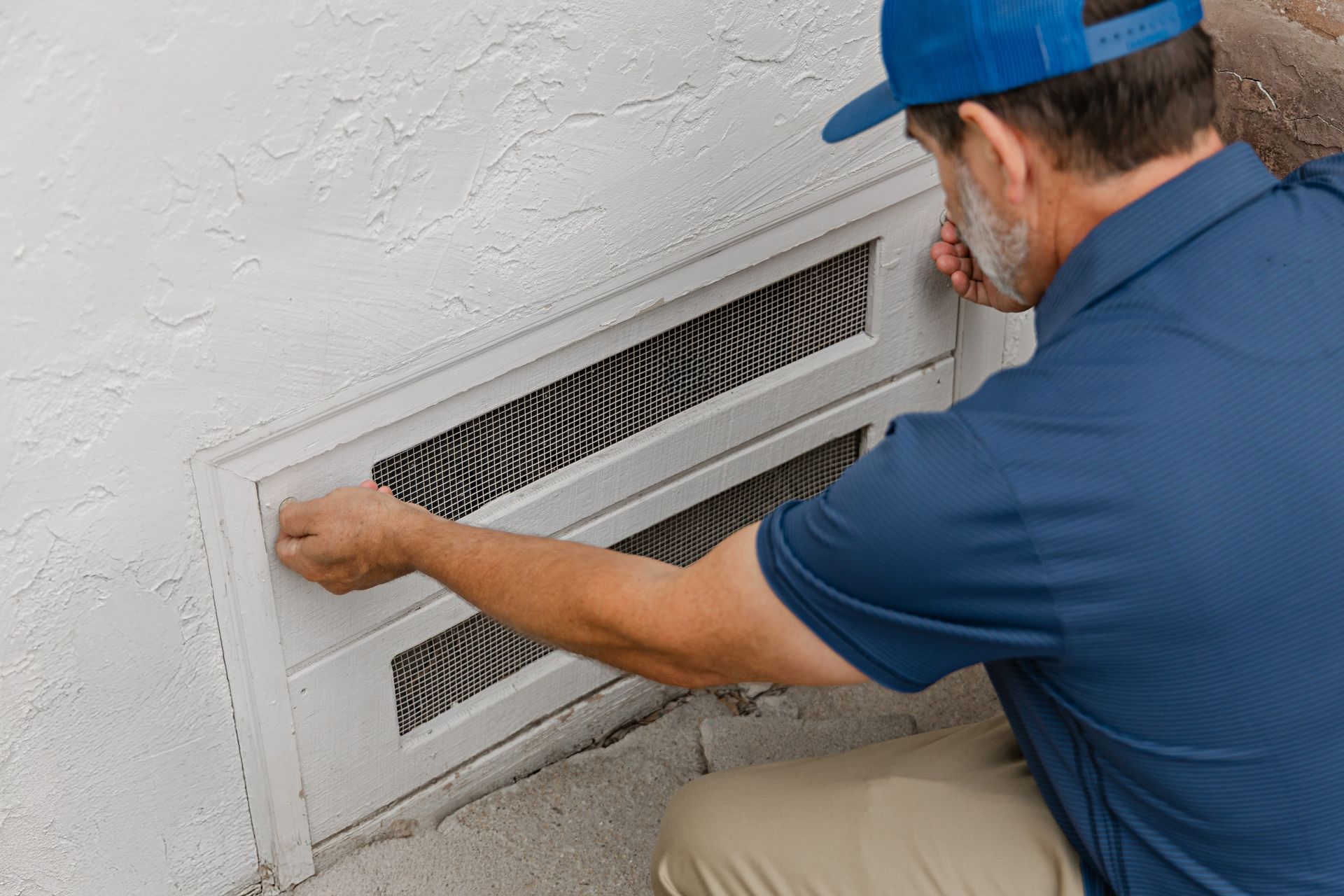 Man installing or adjusting a white wall vent cover with a blue cap on a light textured wall Man installing or adjusting a white wall vent cover with a blue cap on a light textured wall