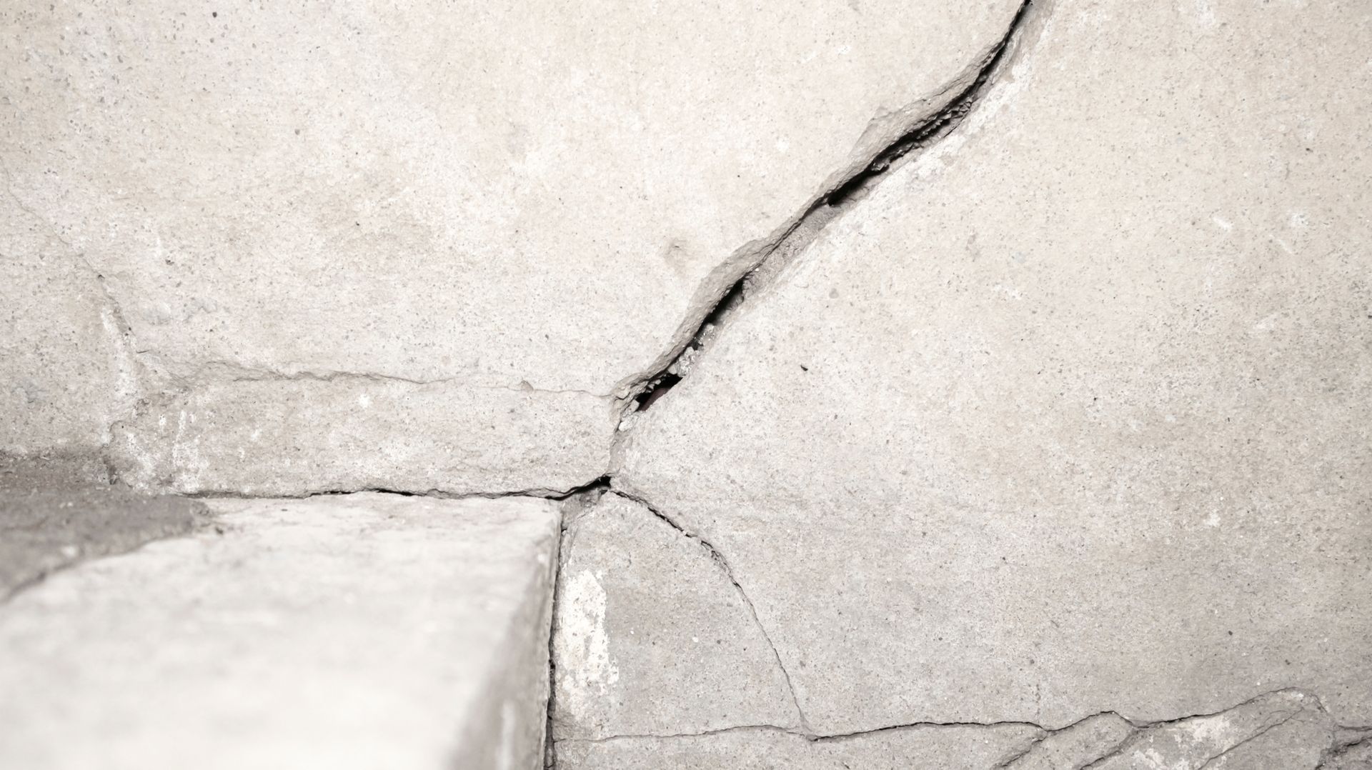 structural damage on a beige plaster wall beside a window.
