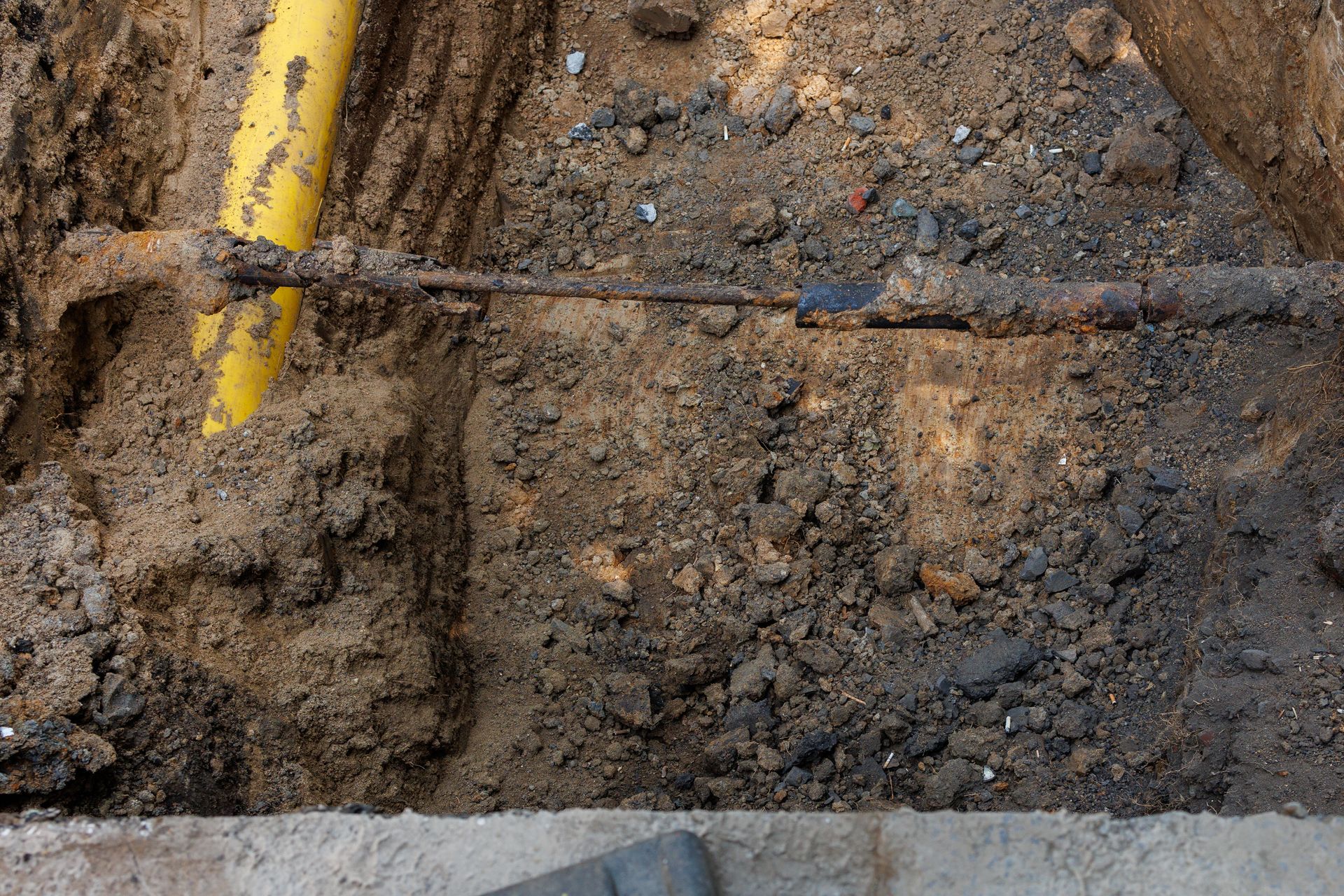 Trench with exposed soil and a yellow utility pipe or marking along the edge.