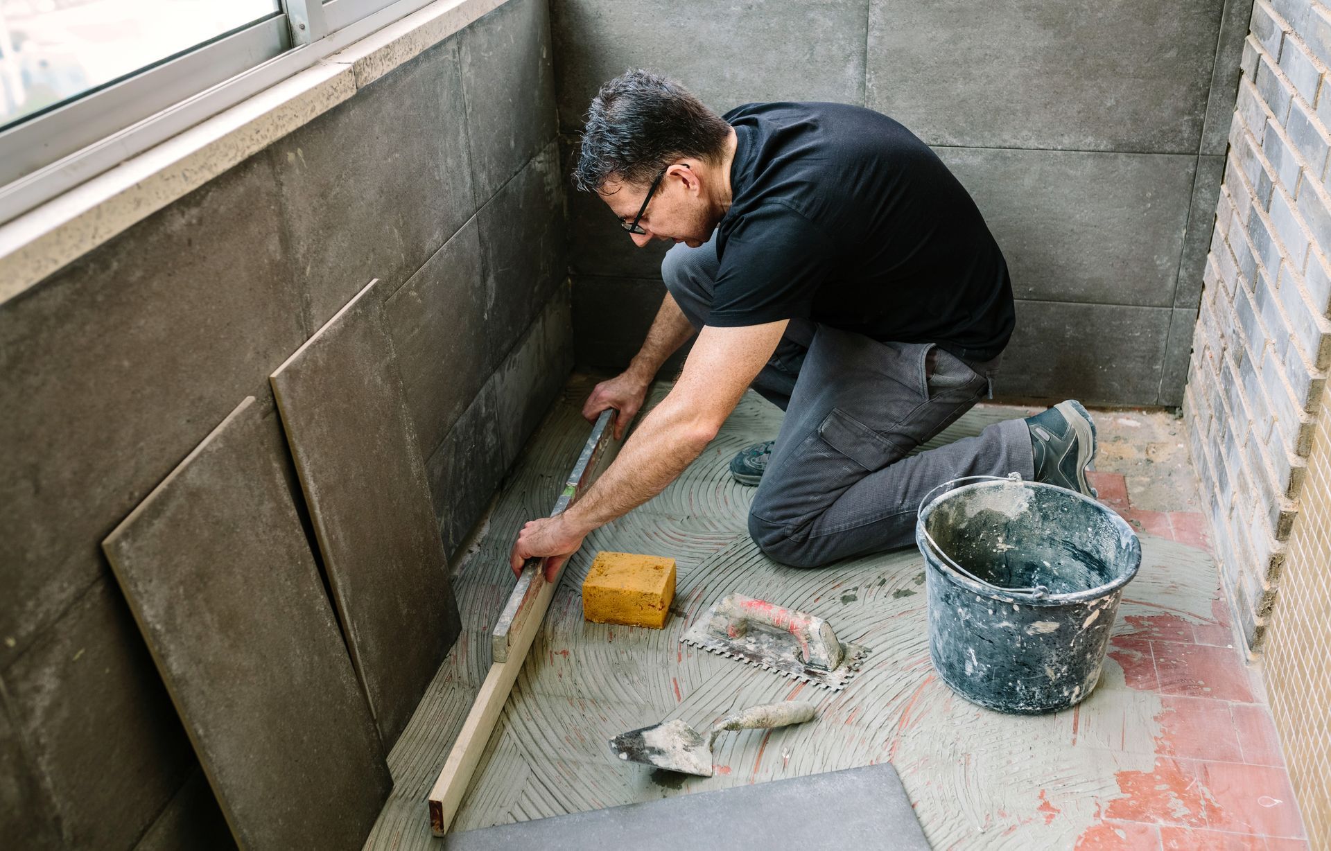 Man kneeling and smoothing mortar on a tiled floor in a narrow balcony or patio area Man kneeling and smoothing mortar on a tiled floor in a narrow balcony or patio area