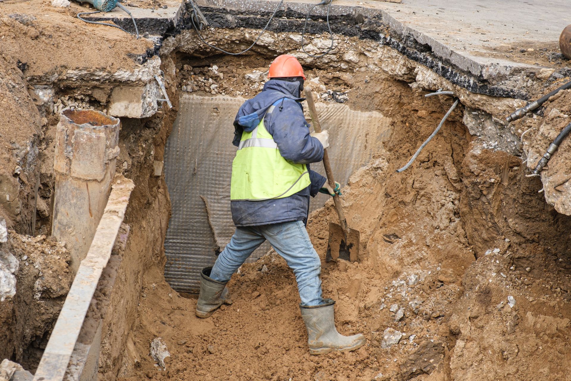 Worker in neon vest and orange hard hat walking through a muddy trench at a construction site